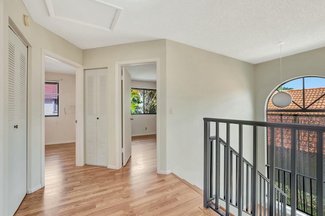 hall with an upstairs landing, light wood-style flooring, a textured ceiling, and baseboards