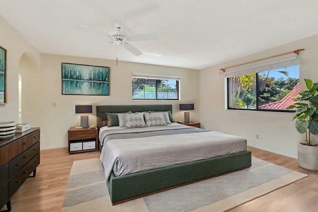 bedroom featuring arched walkways, light wood-style flooring, and ceiling fan