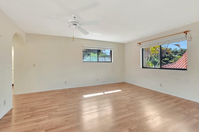 spare room with light wood-style flooring, a ceiling fan, arched walkways, and baseboards