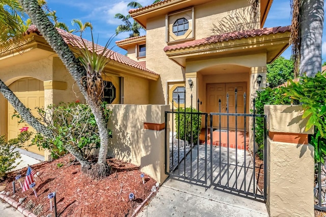 mediterranean / spanish-style house with stucco siding, a tile roof, fence, and a gate