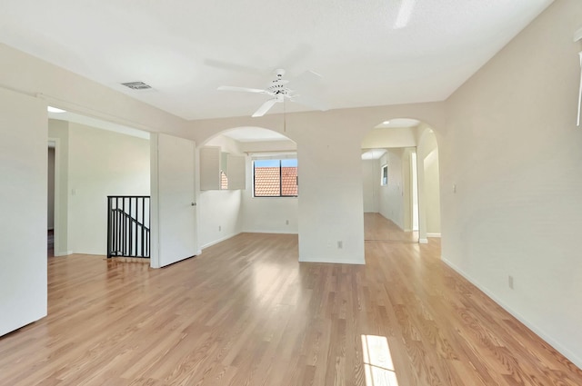 empty room with light wood finished floors, arched walkways, and a ceiling fan