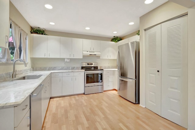 kitchen featuring light stone counters, light wood-style flooring, a sink, under cabinet range hood, and appliances with stainless steel finishes