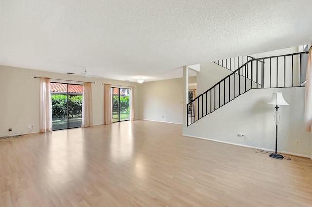 unfurnished living room featuring light wood finished floors, a textured ceiling, stairs, and baseboards