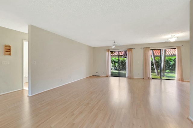 empty room featuring baseboards, light wood finished floors, and a textured ceiling