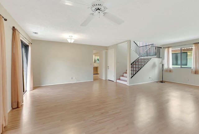 unfurnished living room with stairway, light wood-style floors, visible vents, and ceiling fan