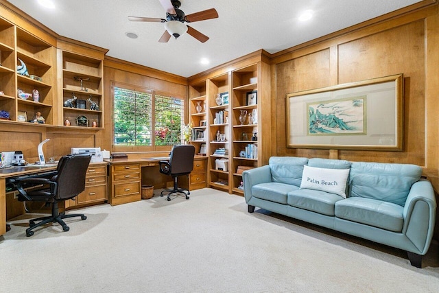 office with built in shelves, ceiling fan, wood walls, light carpet, and built in study area