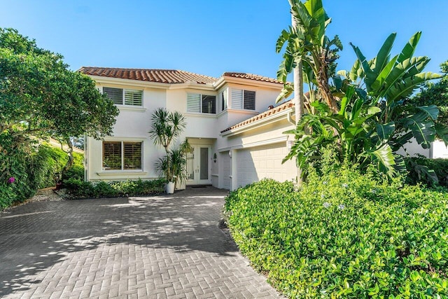 mediterranean / spanish house with an attached garage, stucco siding, french doors, a tile roof, and decorative driveway