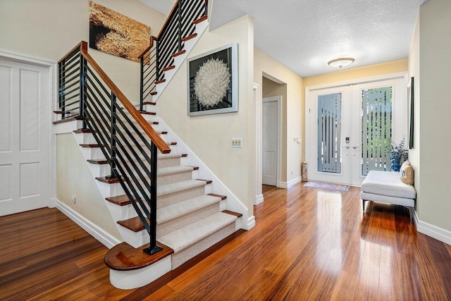 entryway with baseboards, a textured ceiling, wood finished floors, and stairs