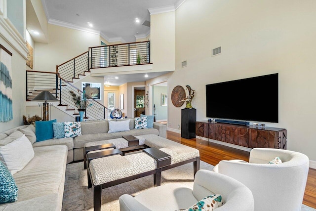 living area featuring stairway, wood finished floors, visible vents, baseboards, and crown molding