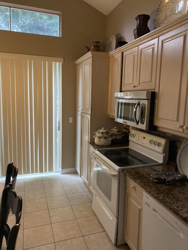 kitchen with white appliances, light tile patterned flooring, dark stone countertops, and lofted ceiling