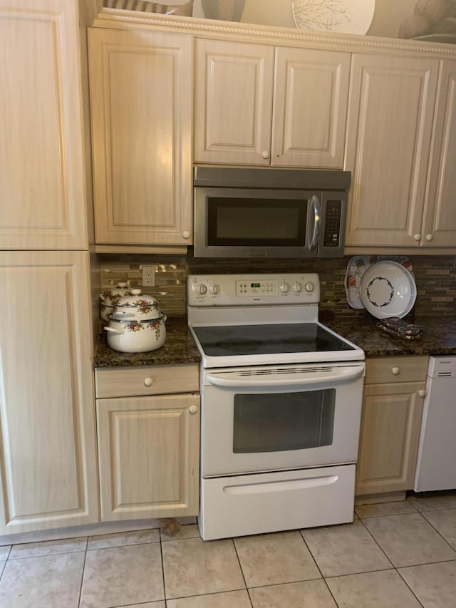 kitchen with light brown cabinetry, dark stone countertops, tasteful backsplash, white appliances, and light tile patterned floors