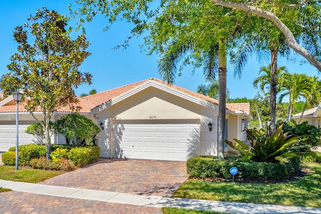 view of front of home featuring a tiled roof, decorative driveway, an attached garage, and stucco siding