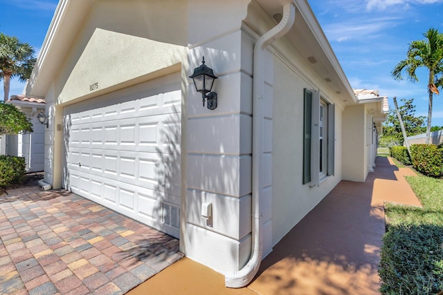 view of side of property featuring stucco siding, a garage, and a tiled roof