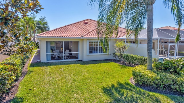 rear view of house featuring a tiled roof, a yard, and stucco siding