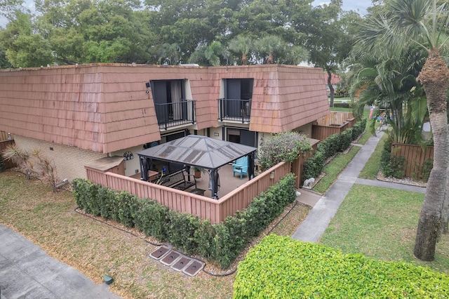 back of house with a gazebo, mansard roof, brick siding, and a balcony