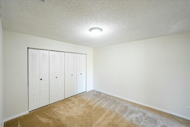 unfurnished bedroom featuring light carpet, baseboards, a textured ceiling, and a closet