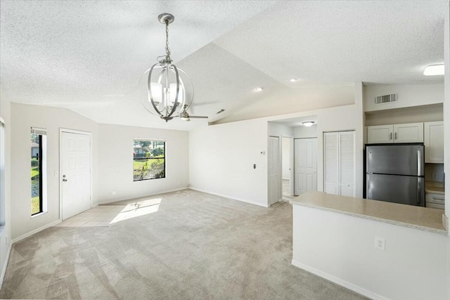 unfurnished living room with an inviting chandelier, vaulted ceiling, light colored carpet, and visible vents