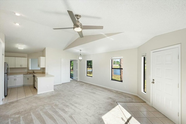 unfurnished living room featuring a sink, ceiling fan, vaulted ceiling, a textured ceiling, and light carpet