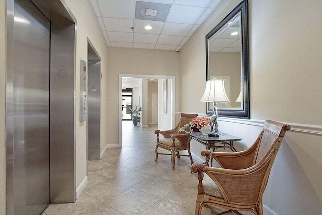 hallway featuring a paneled ceiling, elevator, and light tile patterned flooring