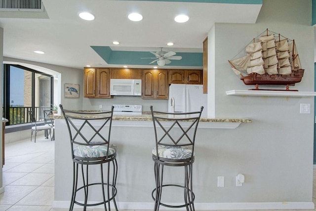 kitchen featuring brown cabinets, white appliances, a breakfast bar area, light tile patterned floors, and ceiling fan