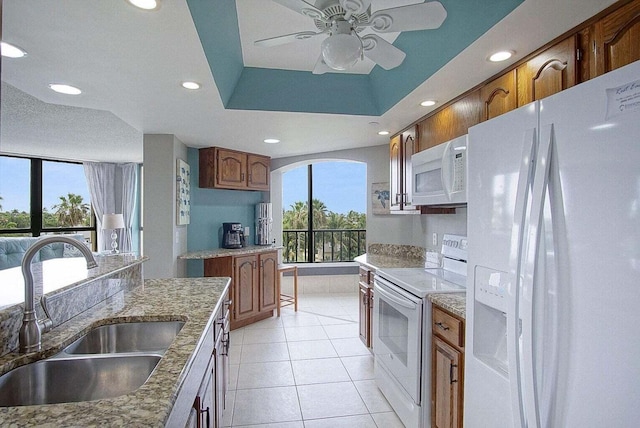 kitchen with a sink, a tray ceiling, recessed lighting, white appliances, and light tile patterned floors