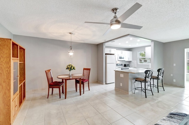 kitchen featuring white appliances, a peninsula, recessed lighting, white cabinetry, and a kitchen breakfast bar