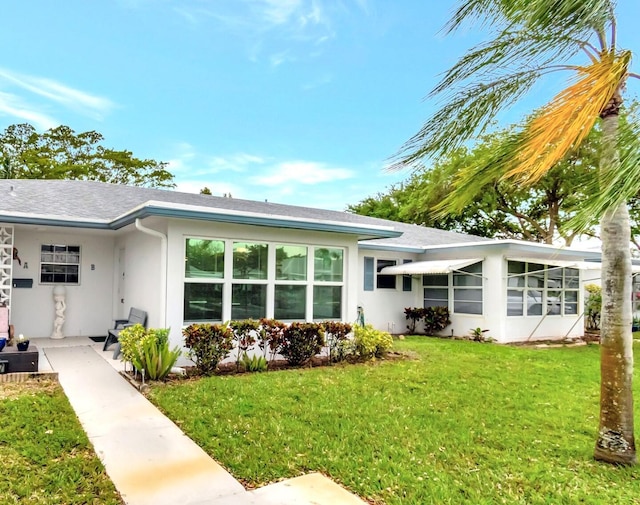 view of front of property featuring stucco siding, a shingled roof, and a front lawn