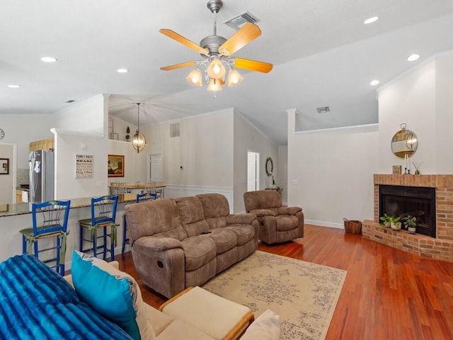 living room with visible vents, ornamental molding, wood finished floors, a fireplace, and vaulted ceiling