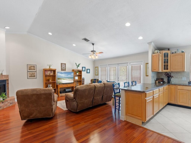 kitchen featuring visible vents, vaulted ceiling, a kitchen breakfast bar, glass insert cabinets, and a brick fireplace