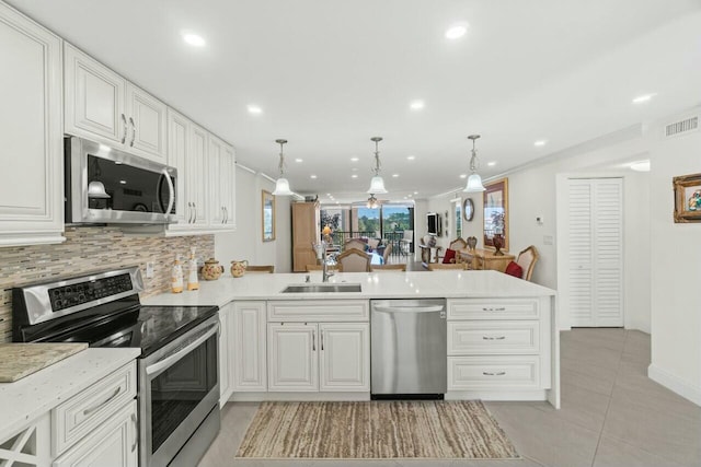 kitchen featuring a peninsula, a sink, light countertops, appliances with stainless steel finishes, and backsplash