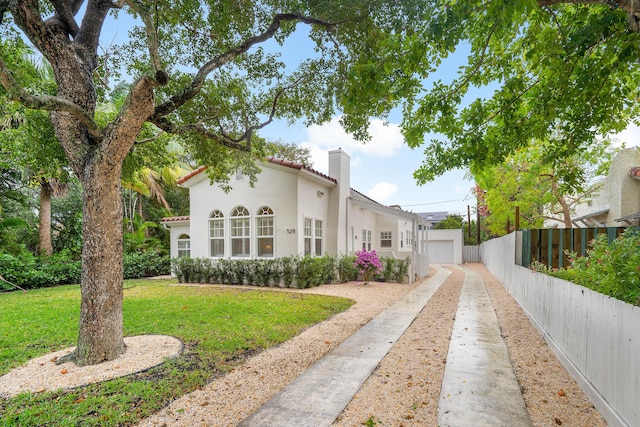 view of front facade with stucco siding, a front lawn, a detached garage, fence, and a chimney