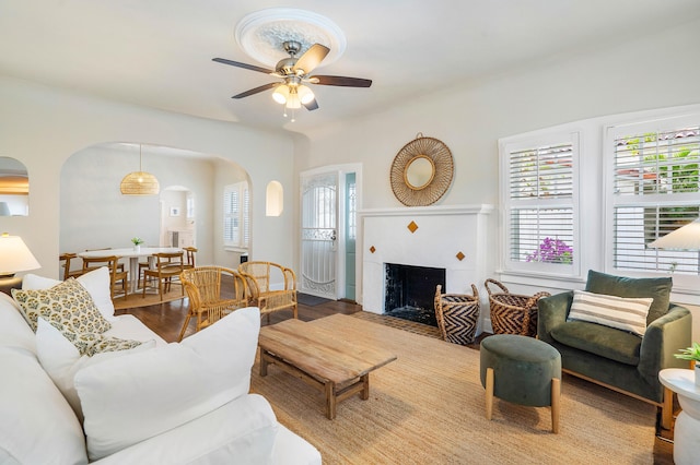 living area featuring arched walkways, a tile fireplace, ceiling fan, and wood finished floors