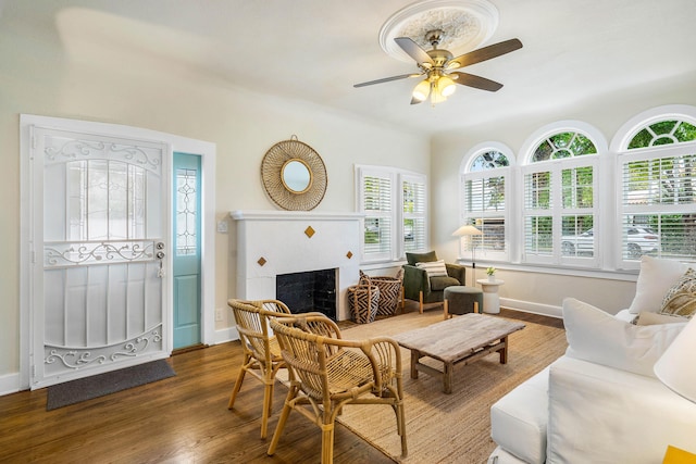 living room with a ceiling fan, a fireplace, dark wood-style flooring, and baseboards