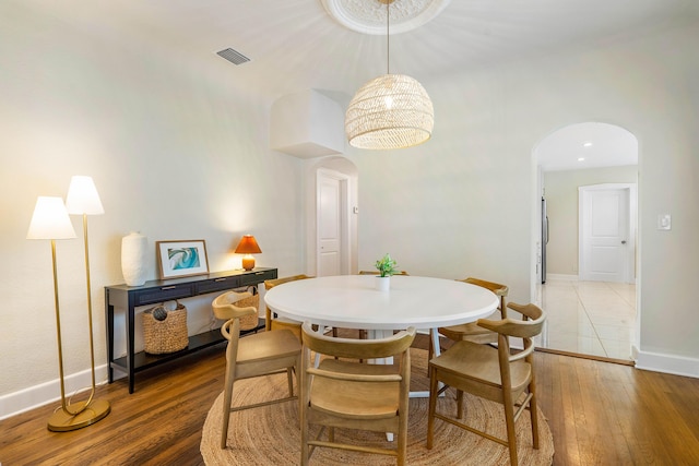 dining space featuring visible vents, baseboards, an inviting chandelier, wood finished floors, and arched walkways