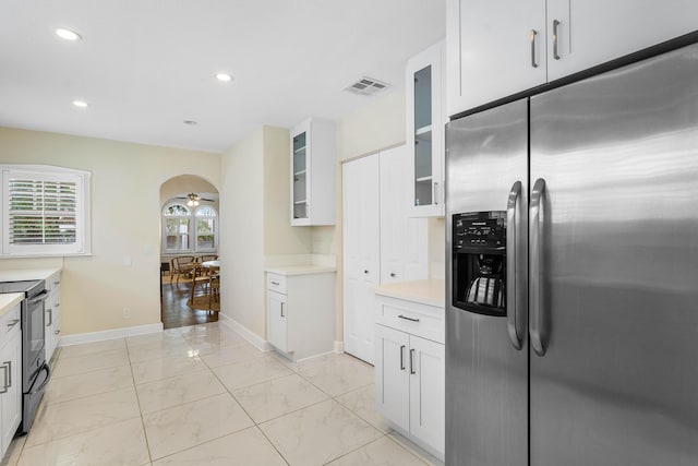 kitchen with marble finish floor, electric range oven, stainless steel fridge, arched walkways, and glass insert cabinets