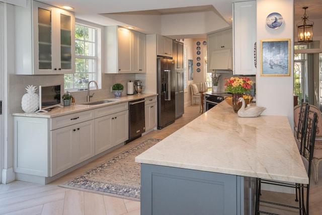 kitchen featuring light stone counters, stainless steel appliances, a sink, glass insert cabinets, and tasteful backsplash