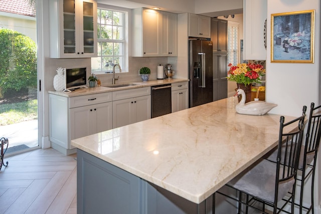 kitchen with a sink, light stone counters, glass insert cabinets, high quality fridge, and decorative backsplash