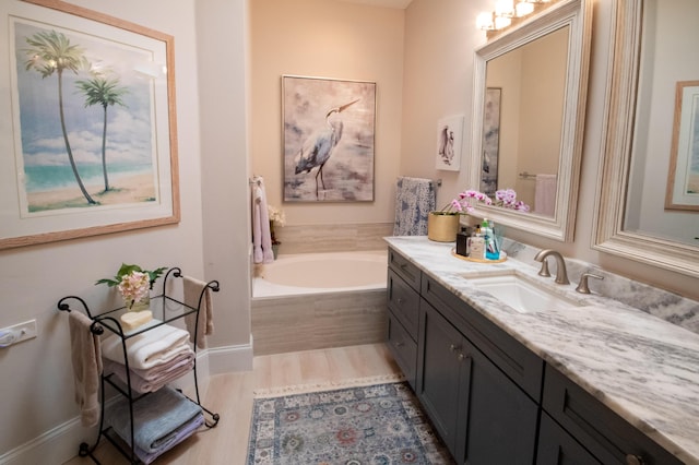 full bathroom with vanity, a bath, wood finished floors, and baseboards