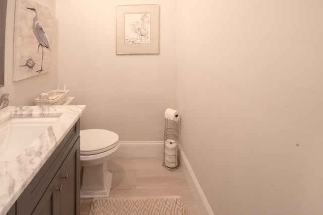 half bathroom featuring baseboards, toilet, and vanity