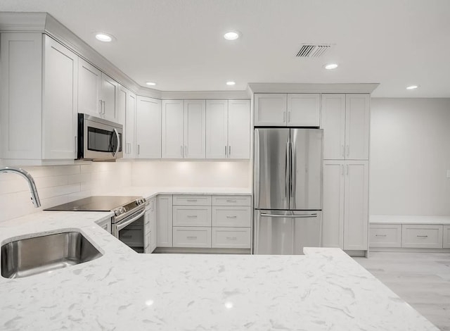 kitchen with visible vents, light stone counters, a sink, tasteful backsplash, and stainless steel appliances