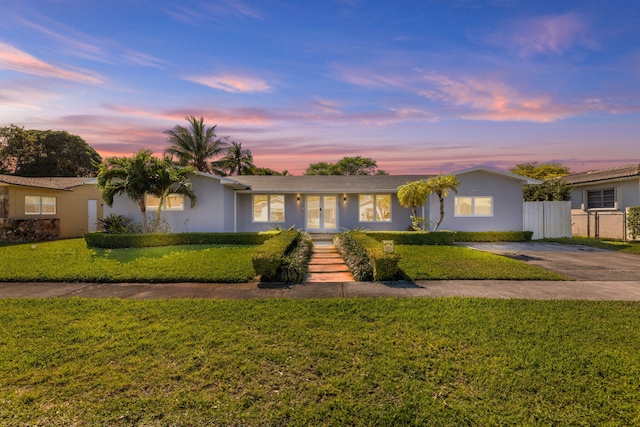 ranch-style home featuring concrete driveway, fence, a front yard, and stucco siding