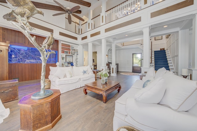 living room featuring stairway, a ceiling fan, wood finished floors, wood walls, and beam ceiling