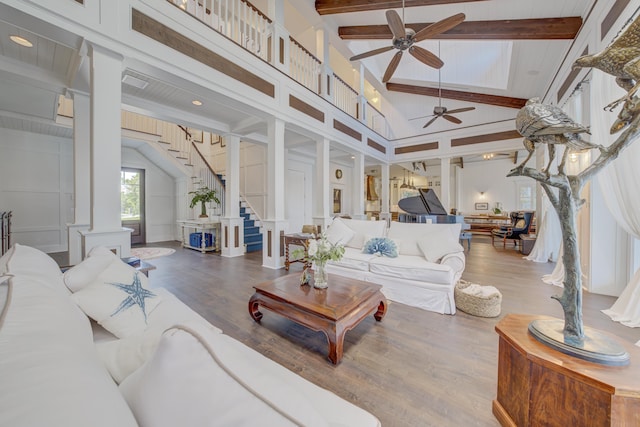 living area with wood finished floors, beam ceiling, a ceiling fan, and stairs