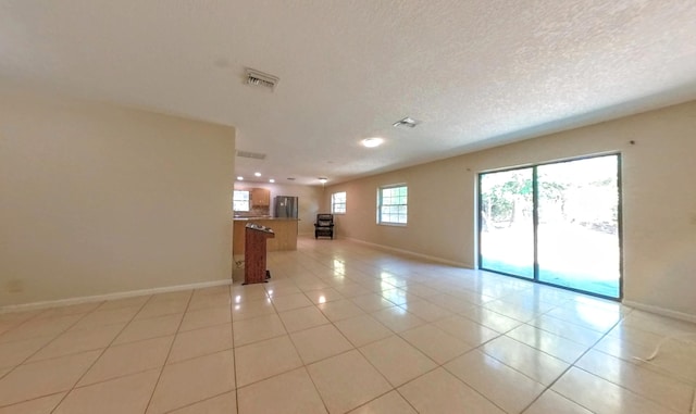 unfurnished room with light tile patterned flooring, visible vents, a textured ceiling, and baseboards