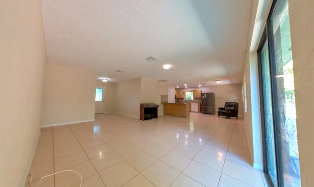 interior space with light tile patterned flooring, visible vents, a textured ceiling, and baseboards