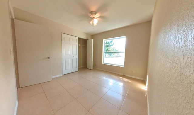 unfurnished bedroom with light tile patterned flooring, ceiling fan, baseboards, and a closet