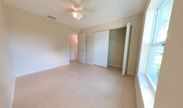 unfurnished bedroom with visible vents, a closet, light tile patterned floors, baseboards, and ceiling fan