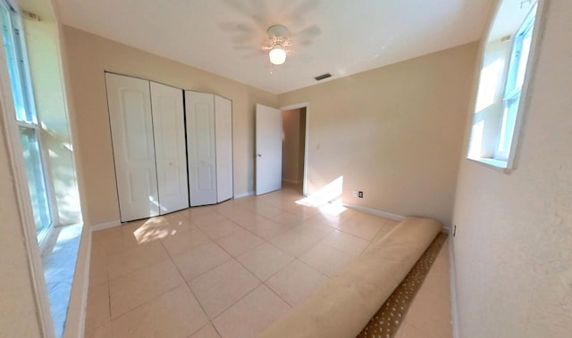 unfurnished bedroom with visible vents, a closet, light tile patterned flooring, baseboards, and ceiling fan