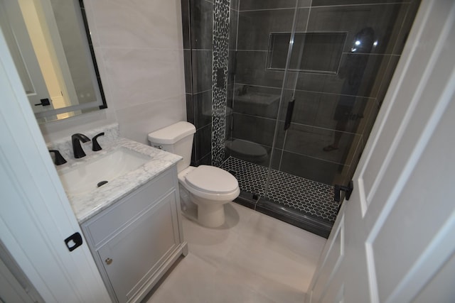 bathroom with tile walls, a stall shower, toilet, and vanity