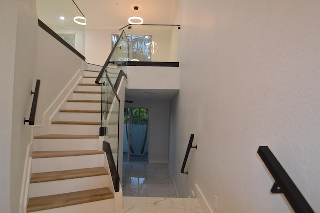 stairway with a healthy amount of sunlight, marble finish floor, a towering ceiling, and baseboards